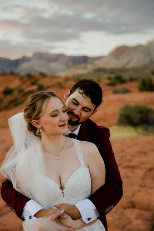 Newlyweds share intimate moment against stunning red rock desert landscape at sunset.