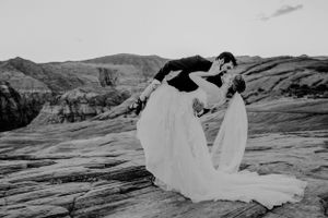Black and white wedding photo of couple in dramatic pose on rock formation.