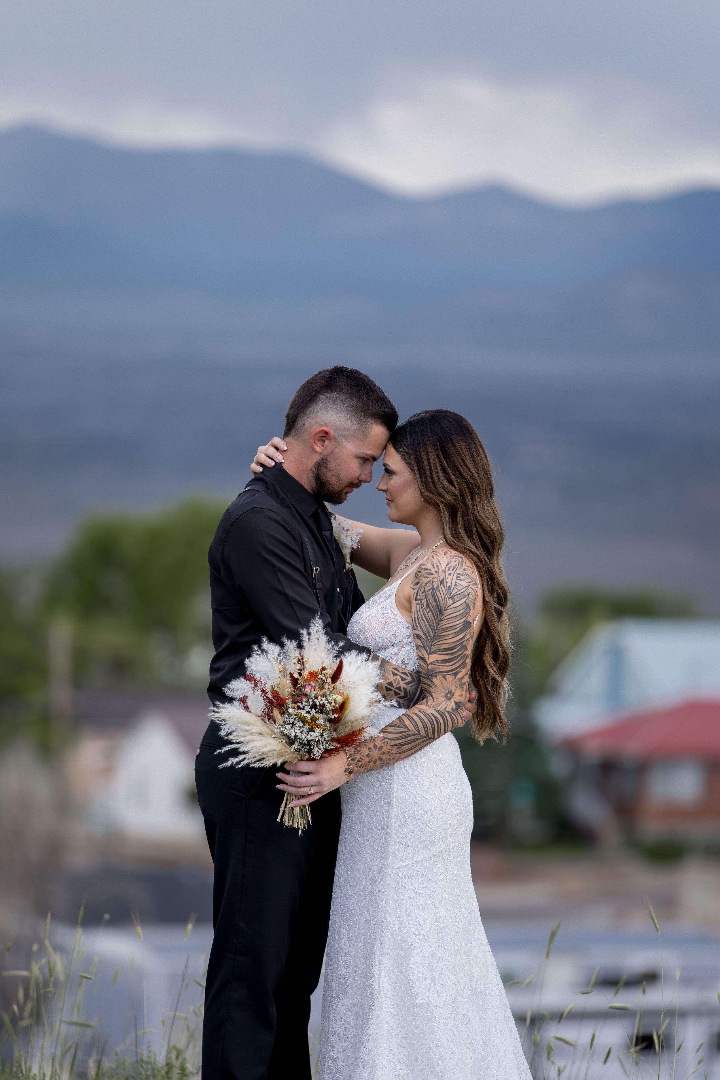 A couple in wedding attire share an intimate moment against a mountain landscape backdrop.