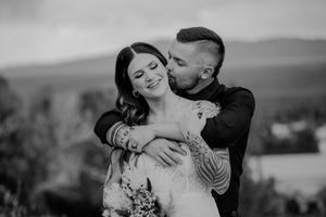 A romantic couple shares an intimate kiss while holding a bouquet during their black and white wedding photoshoot.