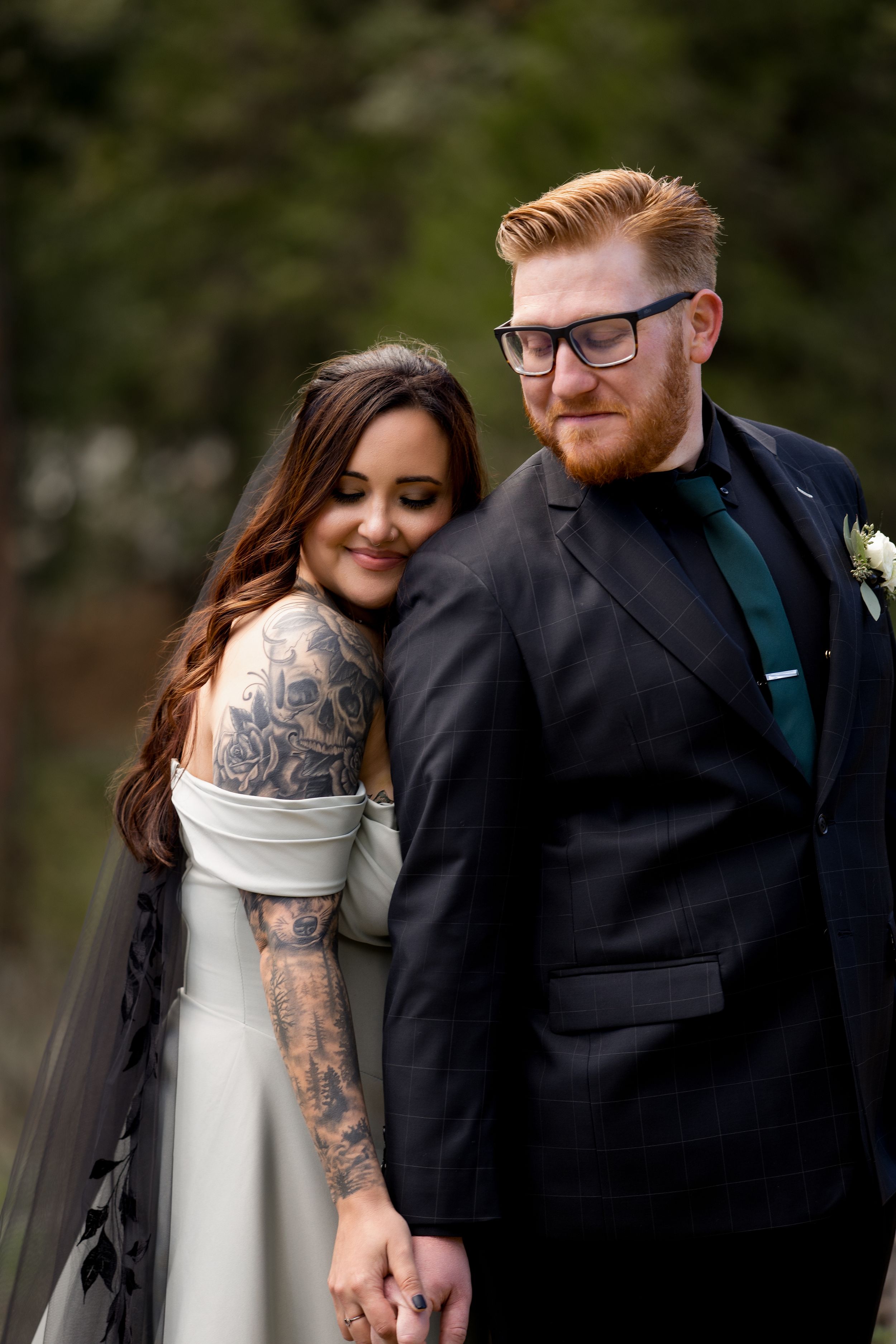 A couple in winter attire embraces outdoors, with the person on the left showing visible arm tattoos through white clothing.