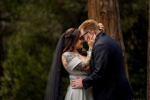 Romantic wedding couple embraces in a scenic forest setting with tall trees in the background.