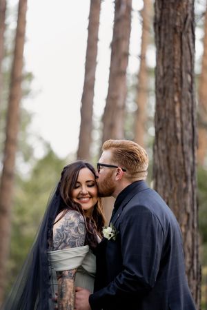 A couple shares an intimate moment among tall pine trees during their outdoor forest wedding ceremony.