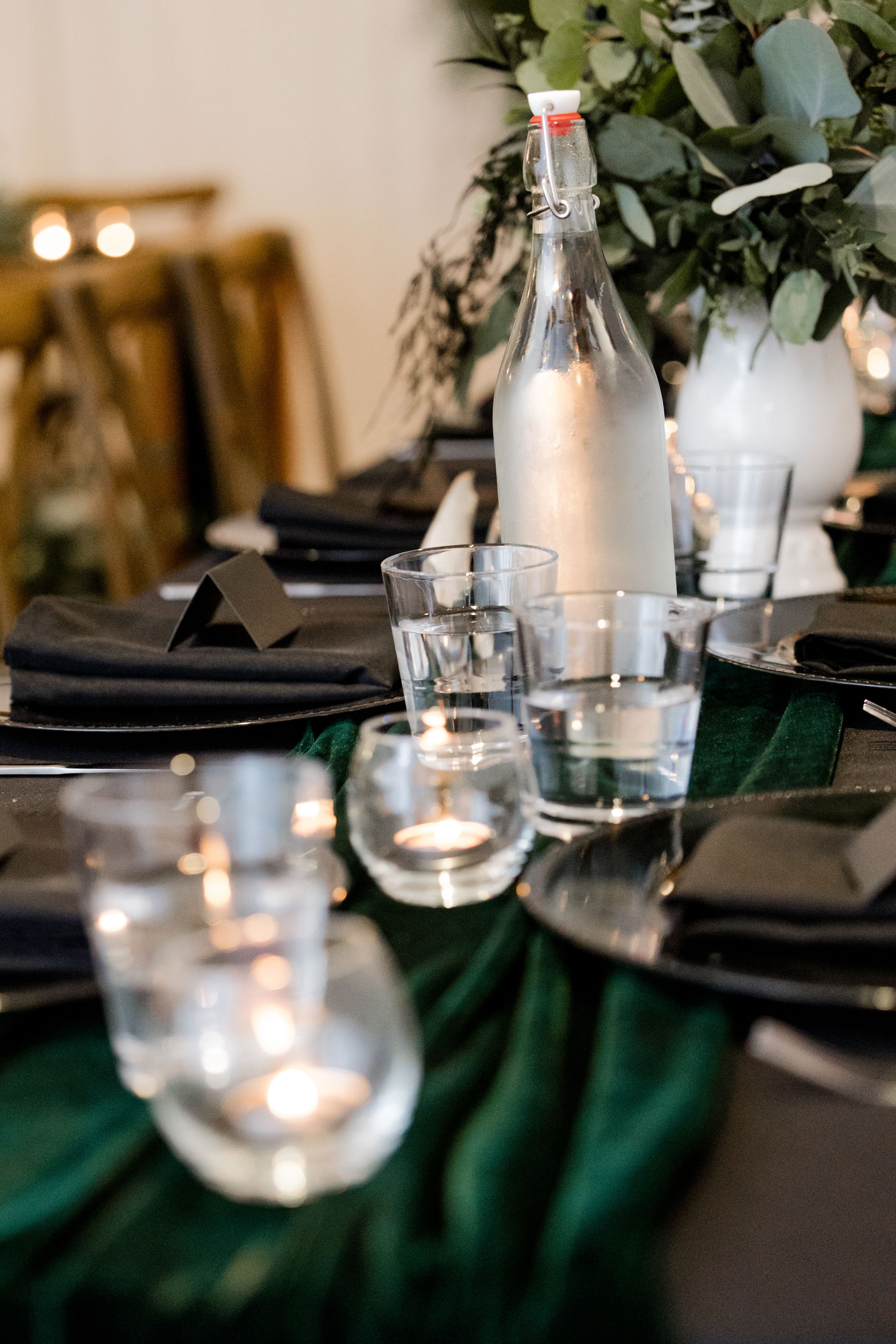 Elegant table setting with black plates, emerald green linens, and glowing candle votives in glass holders.