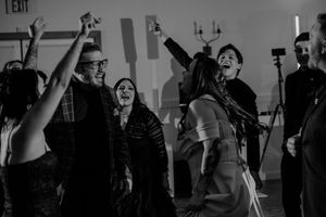 A group of people dancing in a dark studio with an exit sign visible in the background.