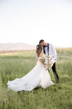 Romantic wedding couple embraces in field at golden hour with flowing white dress.
