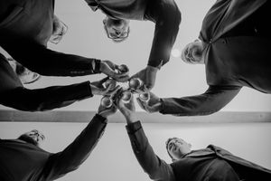 Black and white low angle view of people toasting with beer bottles in a circle formation.