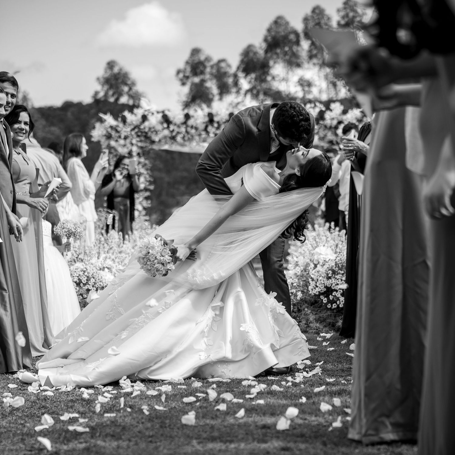 Bride and groom sharing a dramatic dip kiss at outdoor wedding ceremony in black and white.