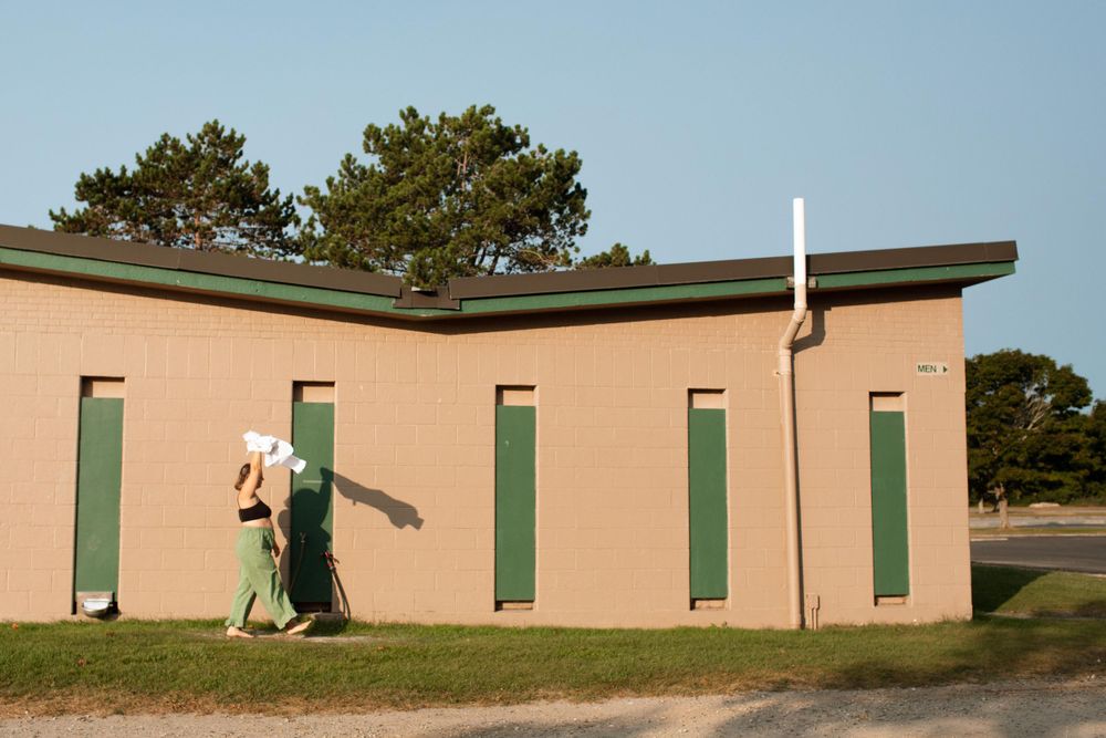Walking figure against beige building with green doors in daylight.