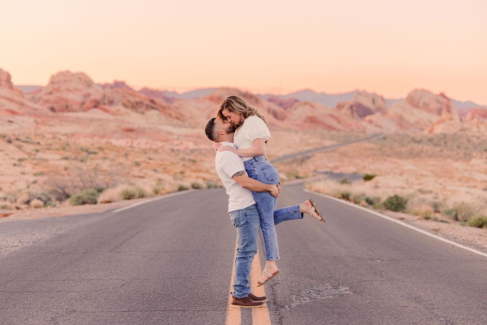 Couple embracing on an empty desert road at sunset with red rock mountains in the background.