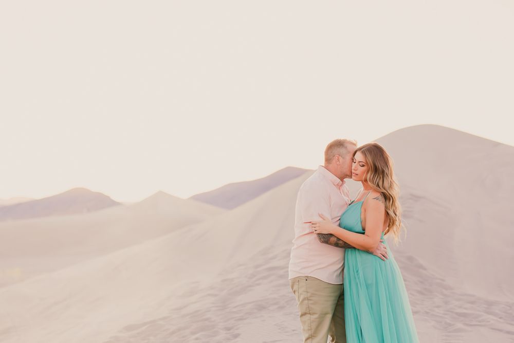 A couple in formal attire embraces on sandy dunes during sunset at Great Sand Dunes National Park.