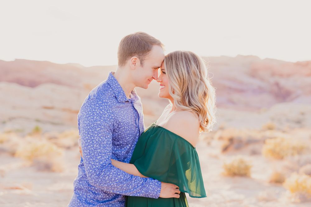 A couple shares a romantic moment in the desert during golden hour with mountains in the background.