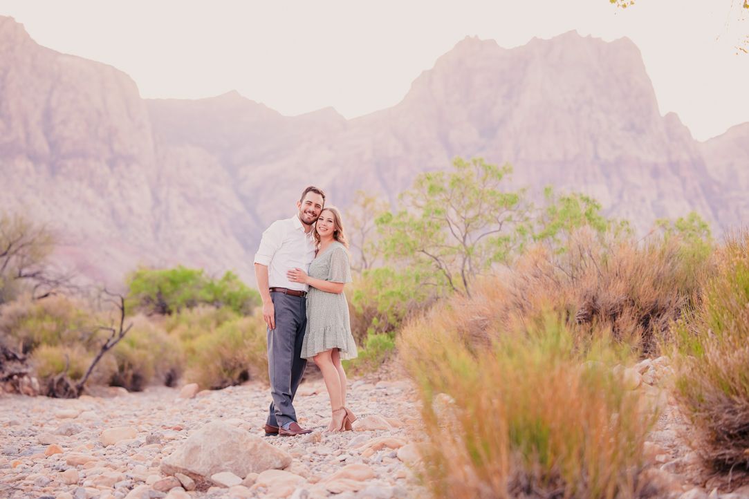 Romantic desert engagement photoshoot with mountains and desert brush in the background during golden hour.