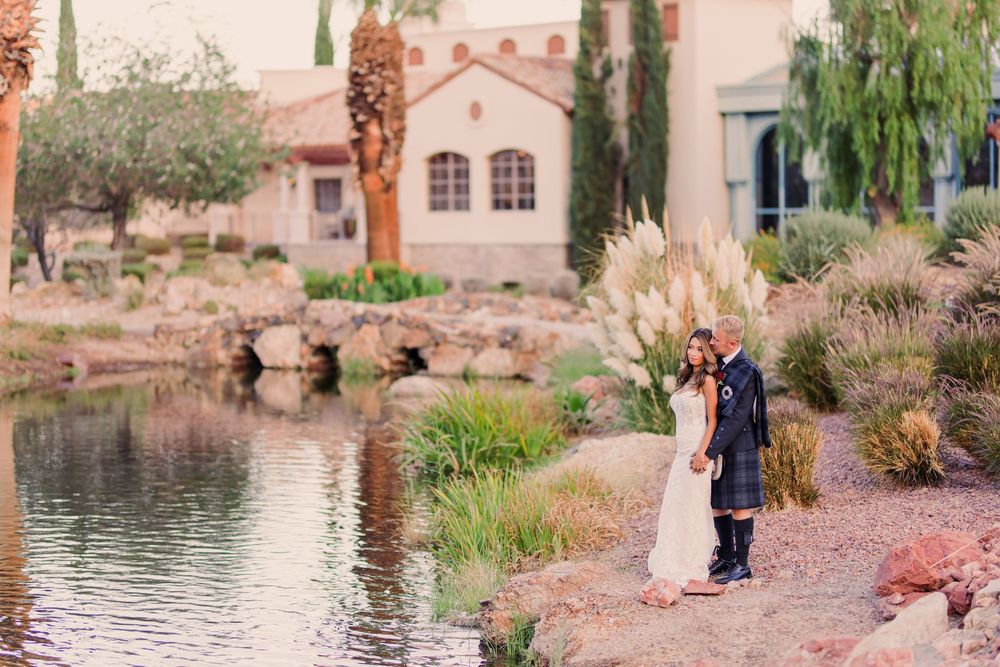 Bride and groom stand by a serene pond surrounded by desert landscaping and pampas grass at an elegant outdoor venue.