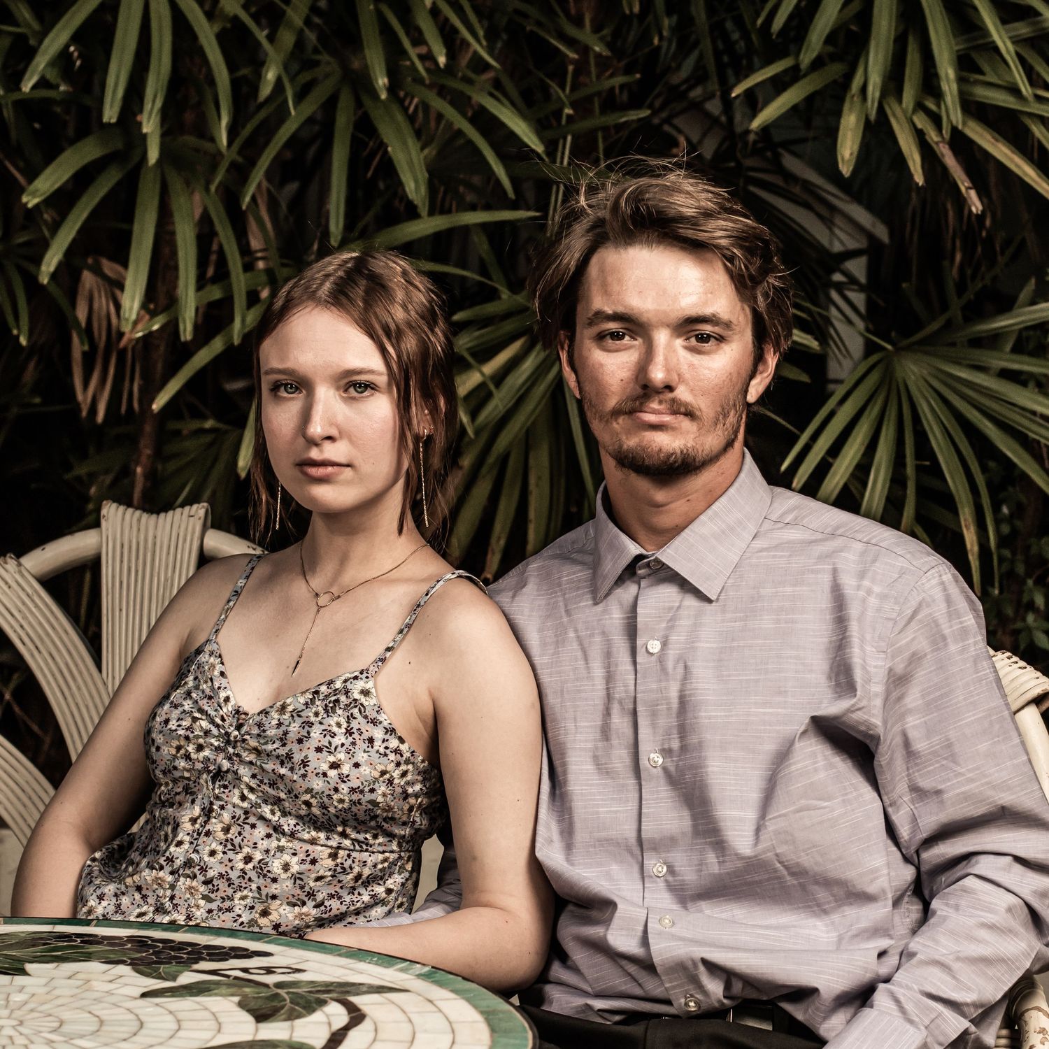 A person in a leopard print dress poses on a bench next to someone wearing a gray shirt.