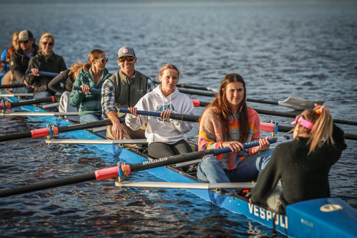 Group of rowers practicing on a recreational team boat at sunset on calm waters.