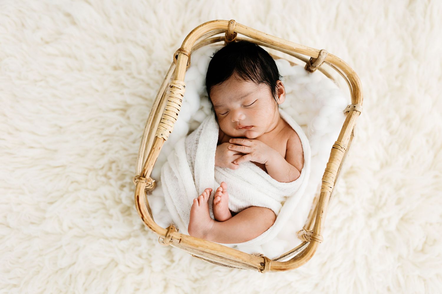 Delicate newborn photography setup with soft pink roses and eucalyptus on white backdrop.