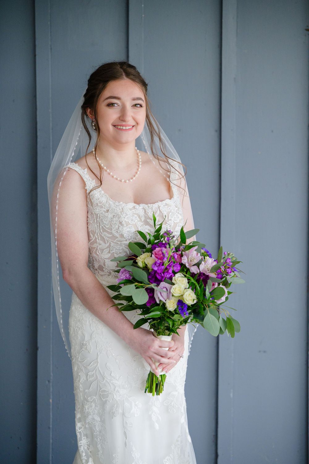 Bride wearing a white tank wedding dress and holding a purple floral bouquet at Brookside Farm in Louisville Ohio shortly before her wedding