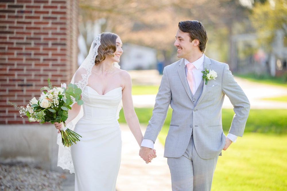 Bride wearing a strapless white gown walking alongside her groom wearing a grey suit with a pink tie at Whitehall Columbia wedding venue
