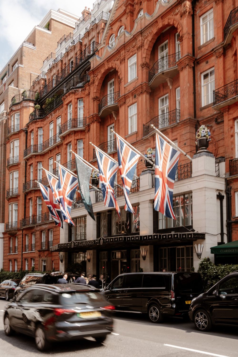 British flags wave outside a classic red brick building in London's upscale Mayfair district as cars pass by.