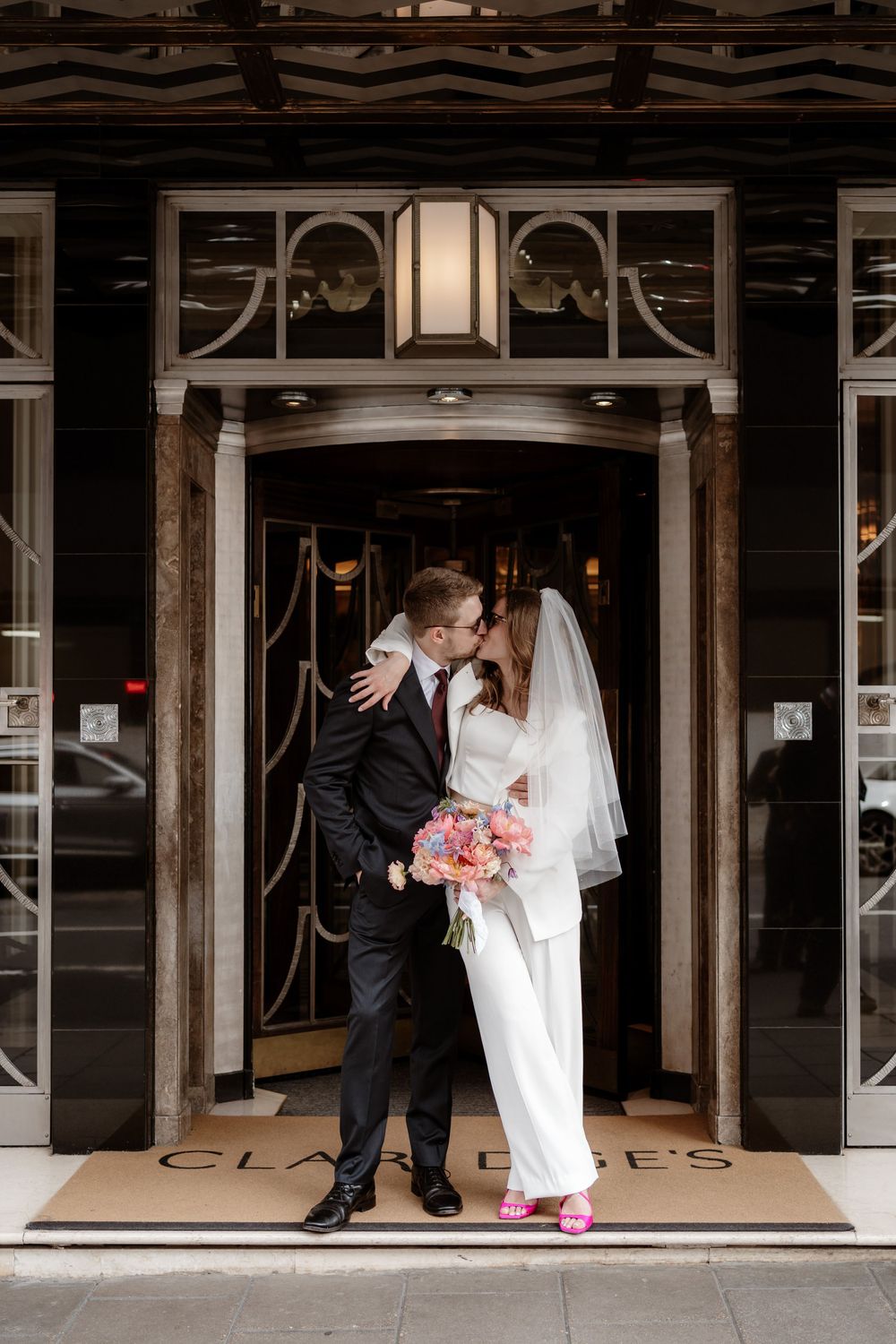 A couple shares an intimate moment in their wedding attire while standing in an elegant doorway entrance.