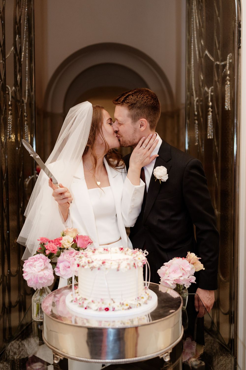 A romantic wedding cake cutting sequence showing a couple sharing sweet kisses beside their pink floral decorated cake.