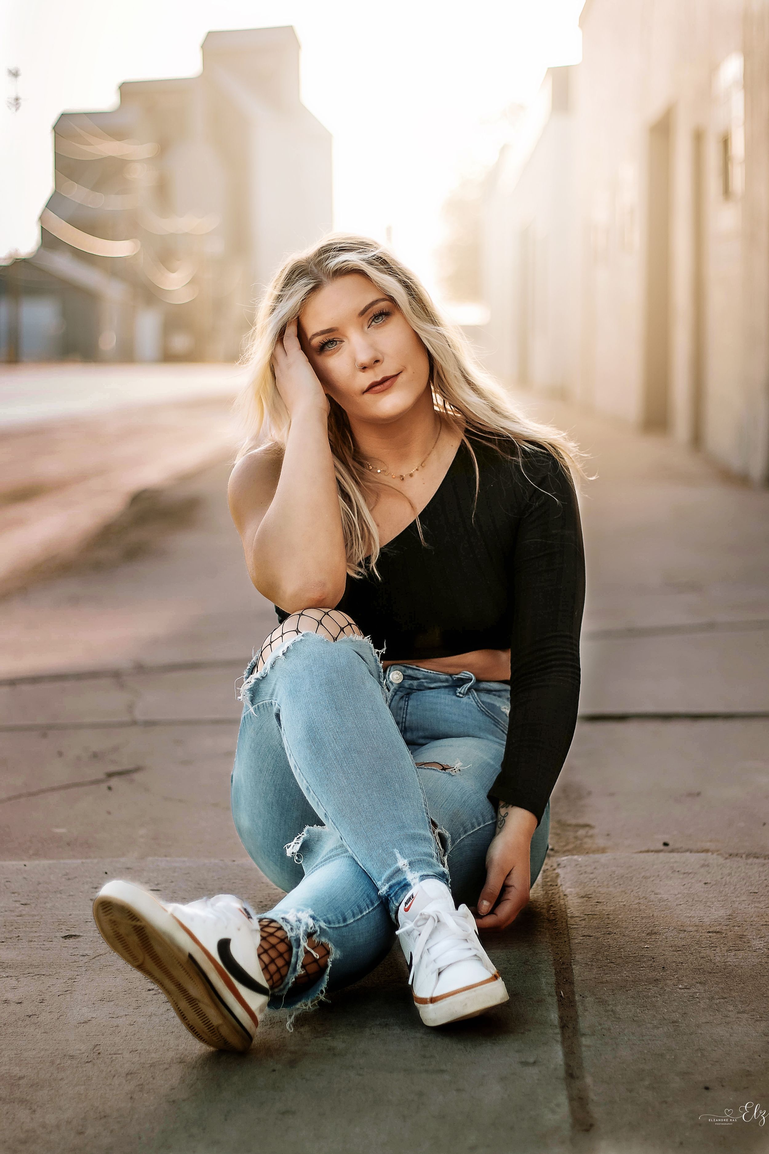 Urban fashion portrait in casual wear sitting against concrete wall in warm sunlight in Williston, North Dakota.