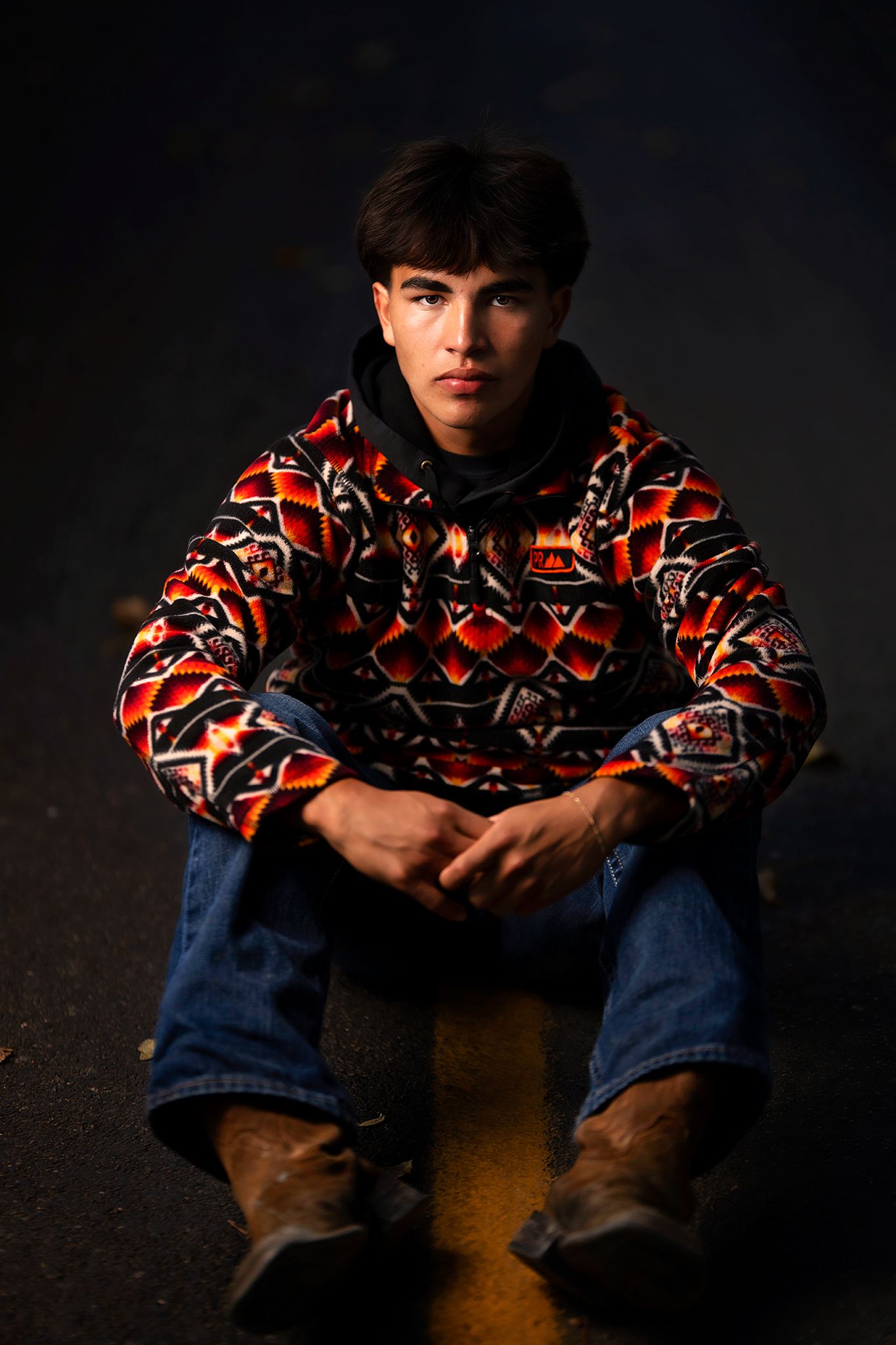 Dramatic portrait in patterned sweater and jeans against dark background in Williston, North Dakota.