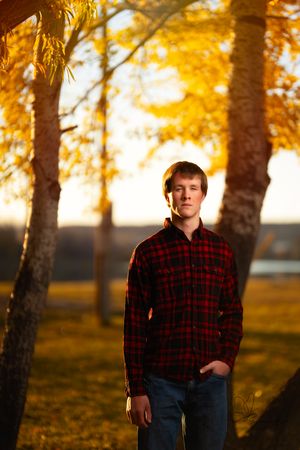 Person in red plaid flannel shirt posing among autumn trees at golden hour in Williston, North Dakota.