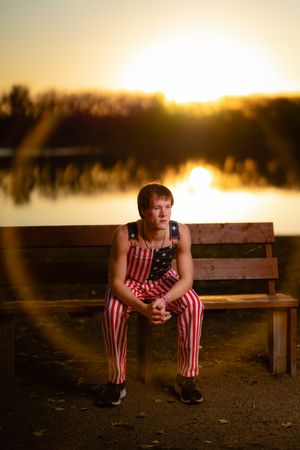 Person in striped outfit sitting on bench at sunset by lake in Williston, North Dakota.