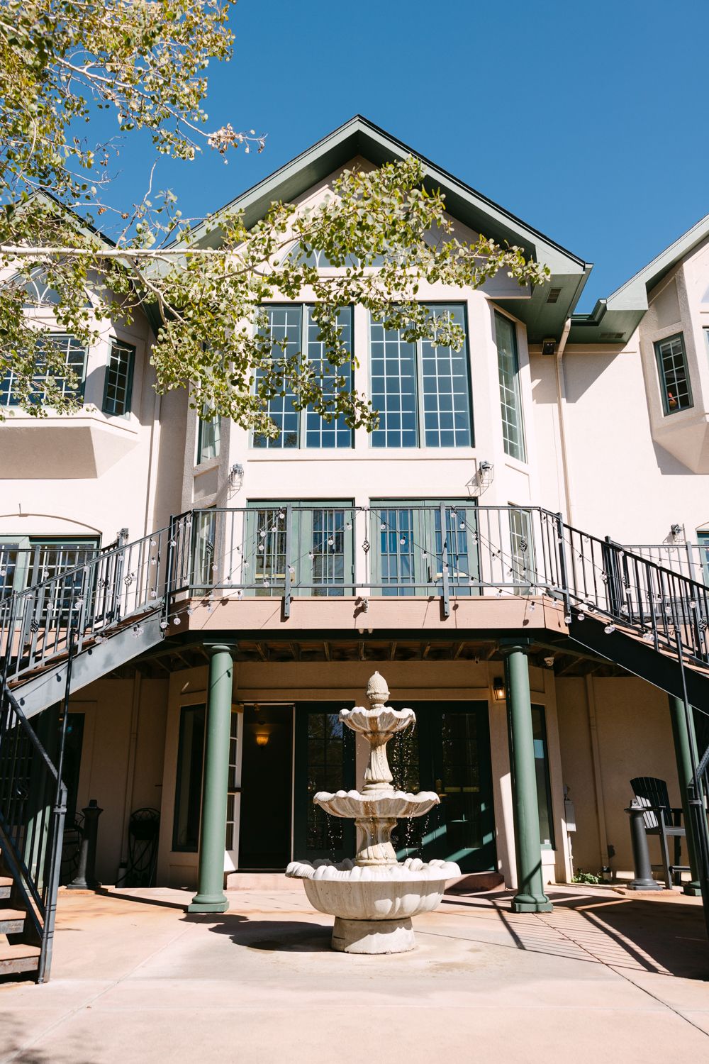 Modern two-story event venue with white exterior, green columns and decorative fountain under blue sky.