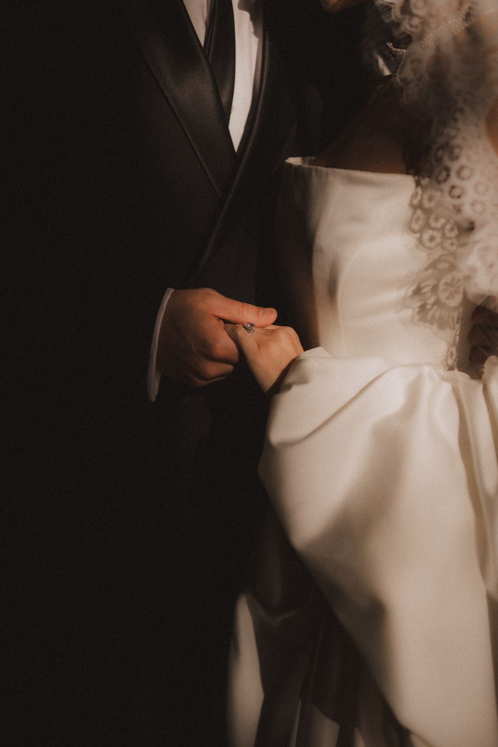 A close-up detail shot of a bride's elegant white wedding dress in dramatic lighting.
