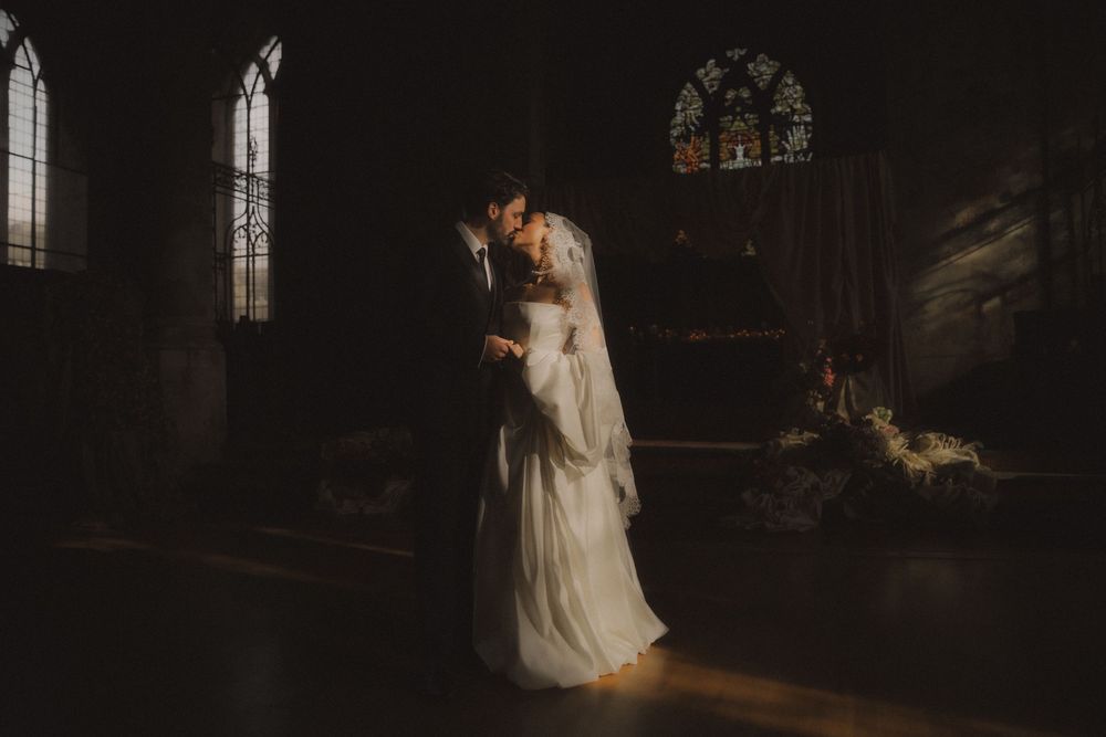 A couple in wedding attire shares an intimate moment in a dimly lit church setting.