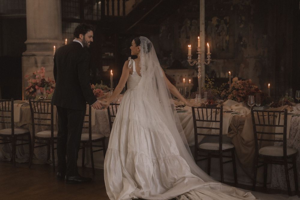 A bride and groom share a romantic first dance in a dimly lit ballroom with candlelit tables.