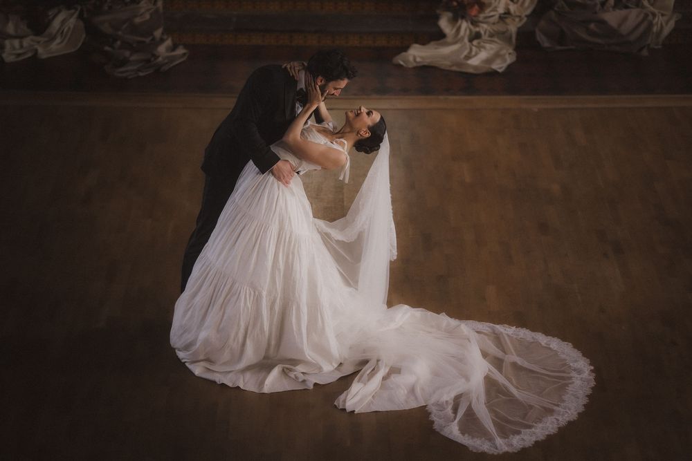A bride in a flowing white wedding dress twirls gracefully on a dark wooden floor during a romantic dance.