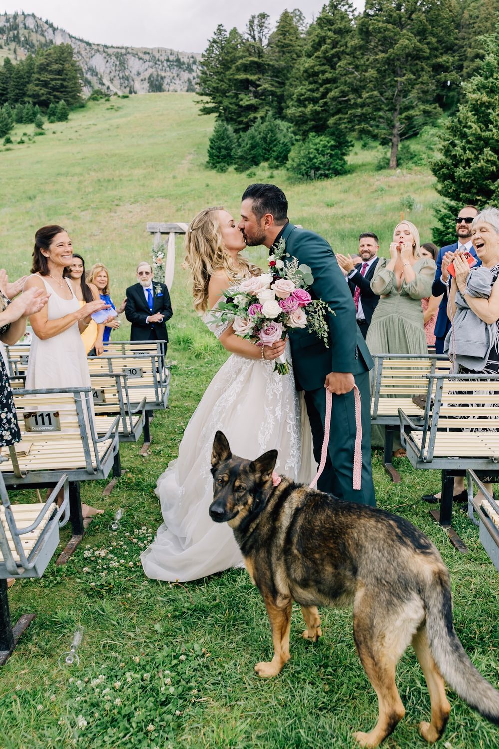 Bride and Groom walking down isle with their dog, with mountain backdrop at the Bridger Bowl Ski Area and Deer park chalet