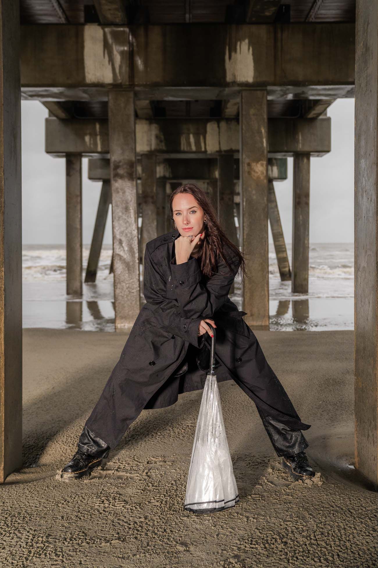 Person in black coat poses under Folly Beach pier  on beach in Charleston, SC.