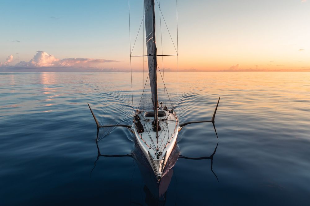 Aerial view of a sailboat on calm ocean waters during a peaceful sunset with golden sky reflections.