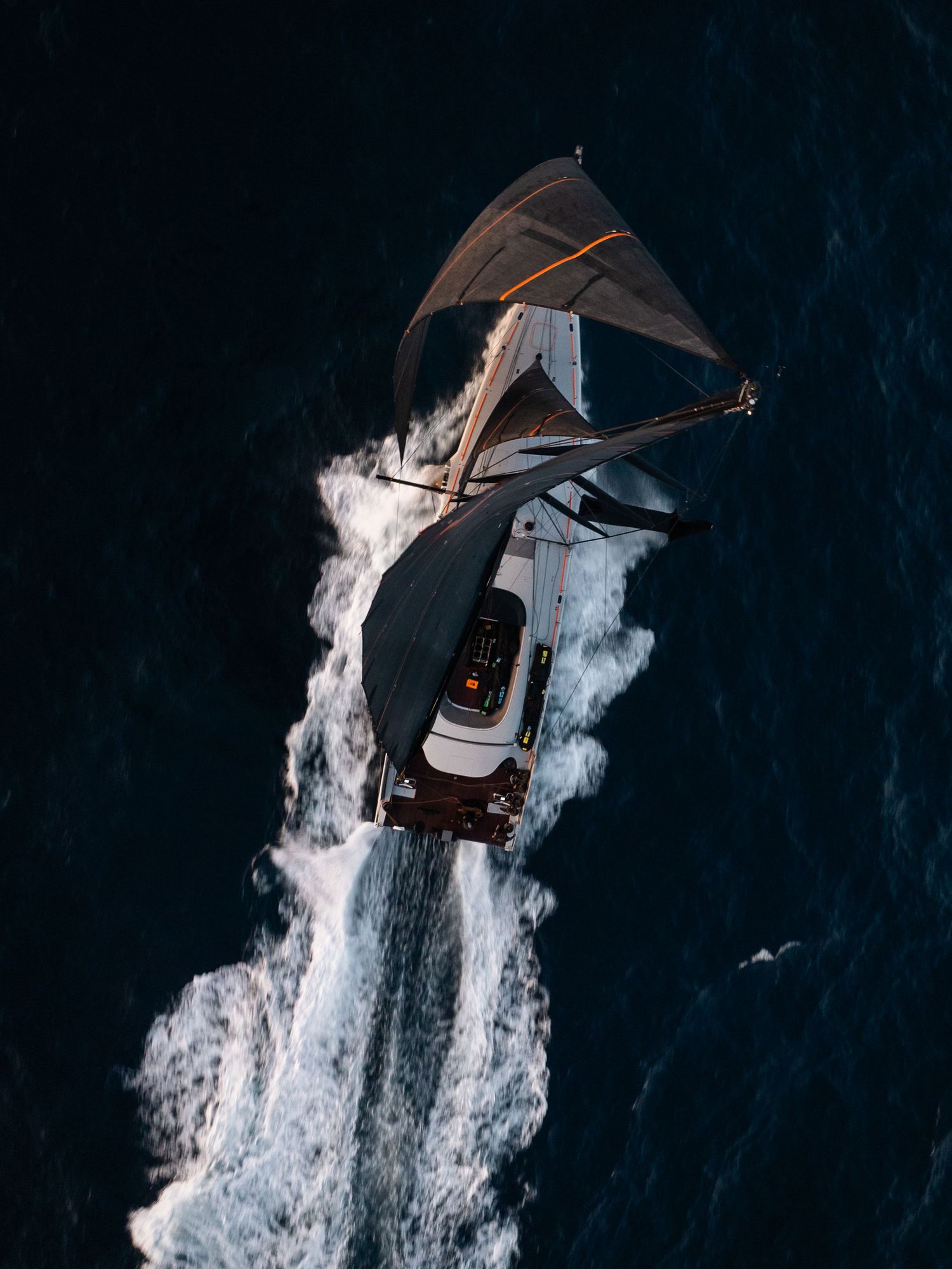 Aerial view of a boat creating a white wake pattern while moving through dark ocean waters.