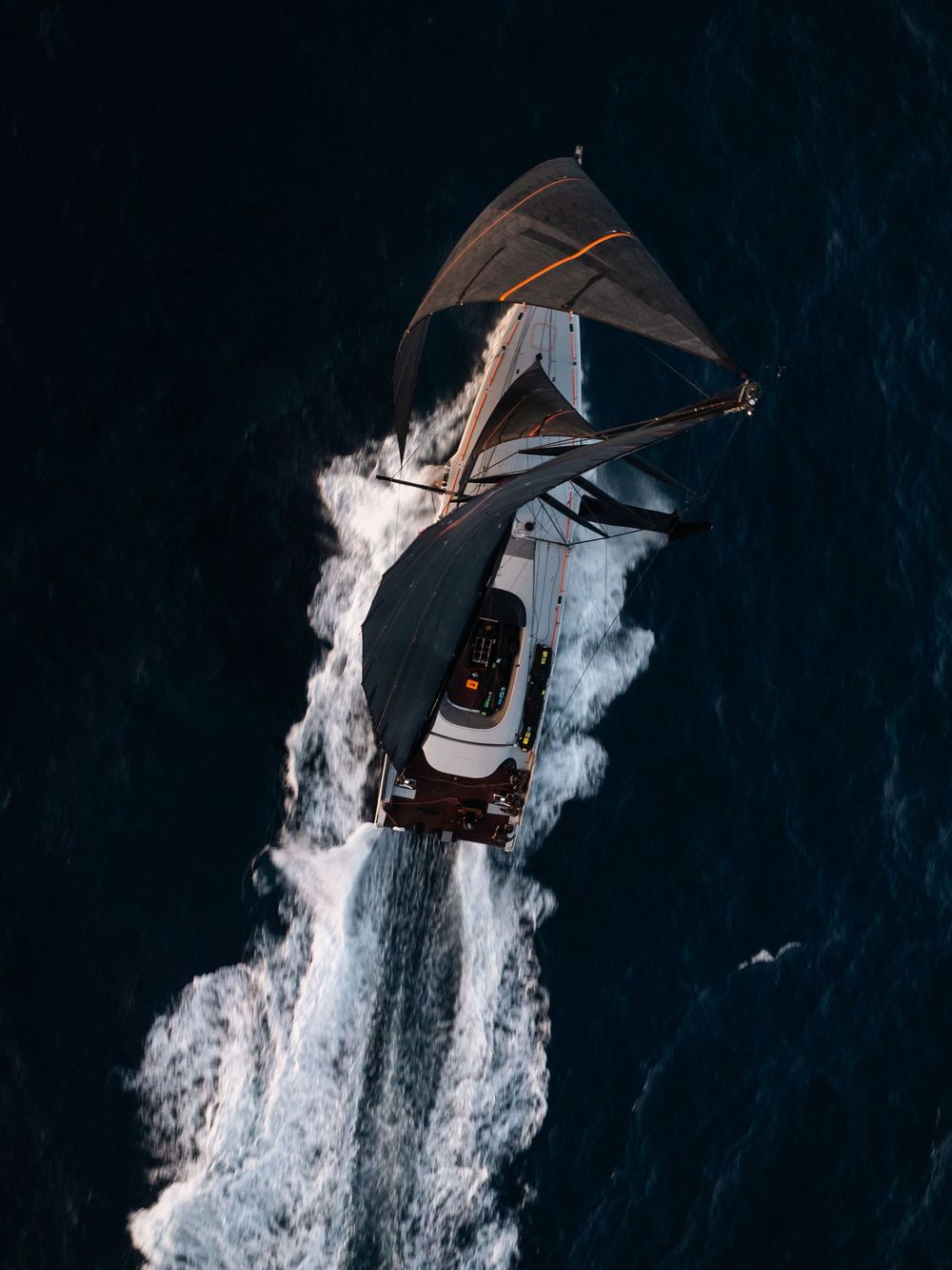 Aerial view of a boat creating a white wake pattern while moving through dark ocean waters.