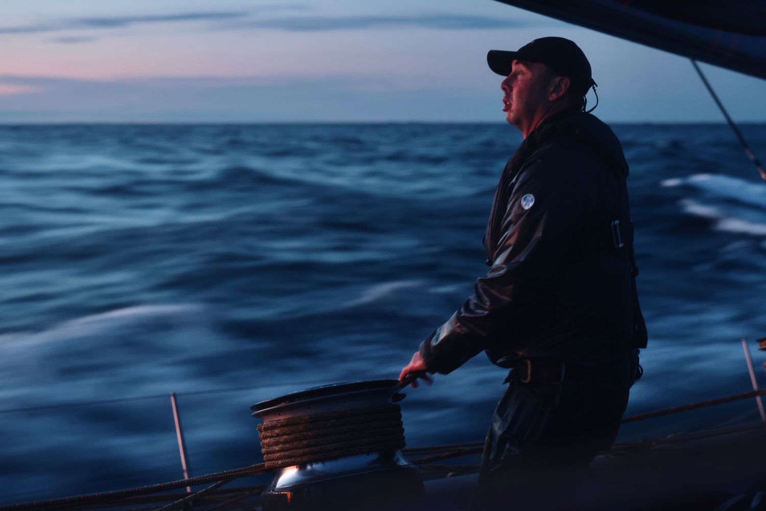 A fisherman casts a line into the blue ocean waters during sunset while standing on a boat.