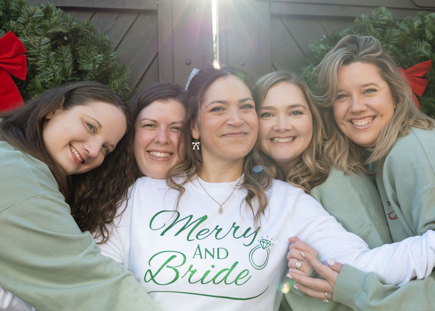 Bride surrounded by bridesmaids wearing matching sweatshirts — candid wedding celebration portrait