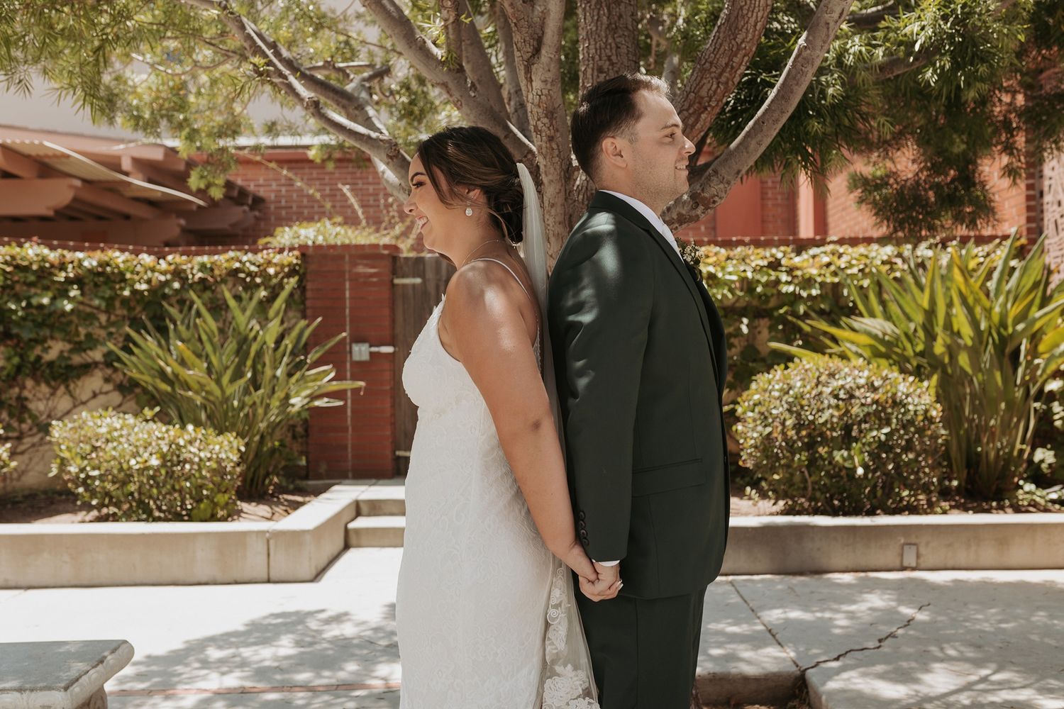 A wedding couple shares a first touch in a lush garden setting during their special day in Escondido, California.