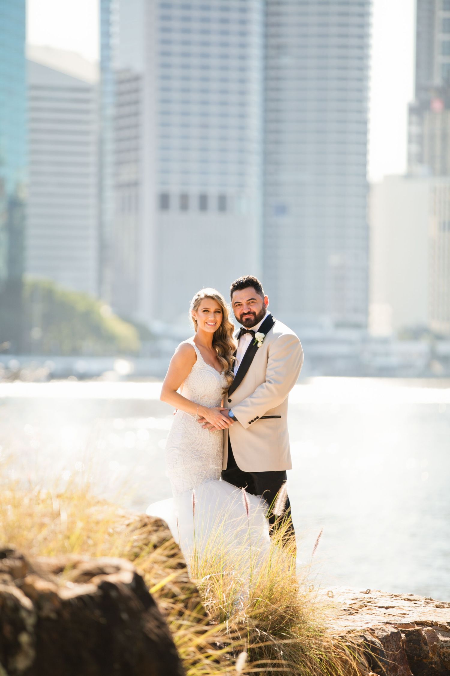 Bride and groom pose romantically by the river with Brisbane city skyline glowing in the background.