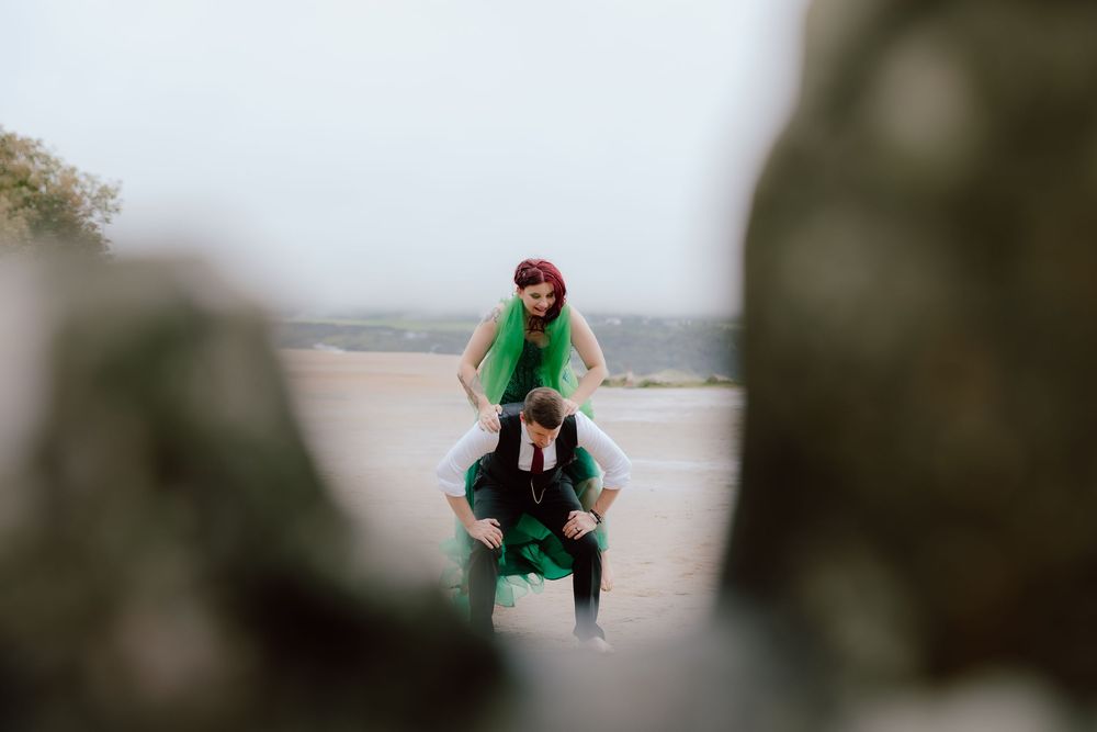 A person wearing a green jacket and hat walks along a foggy coastal path with dramatic cliffs in the background.