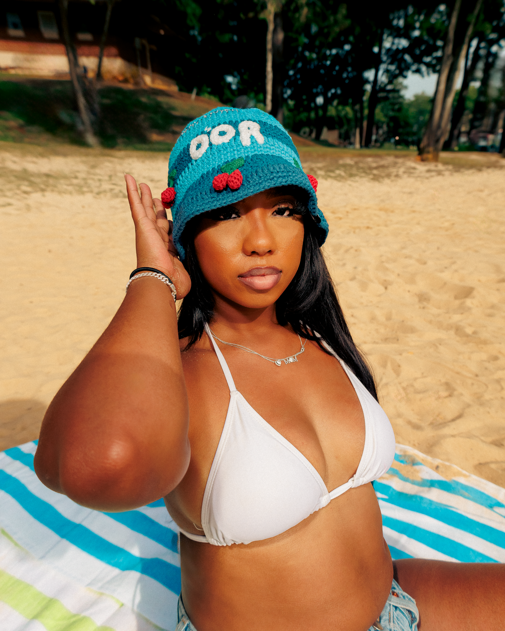 Woman in white bikini and turquoise cap relaxing on striped beach towel at sandy beach.