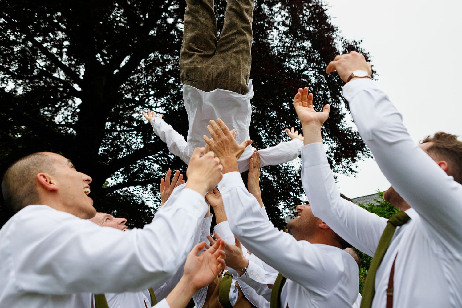 A group of people in white dress shirts raise their drinks in a celebratory toast against a backdrop of trees.