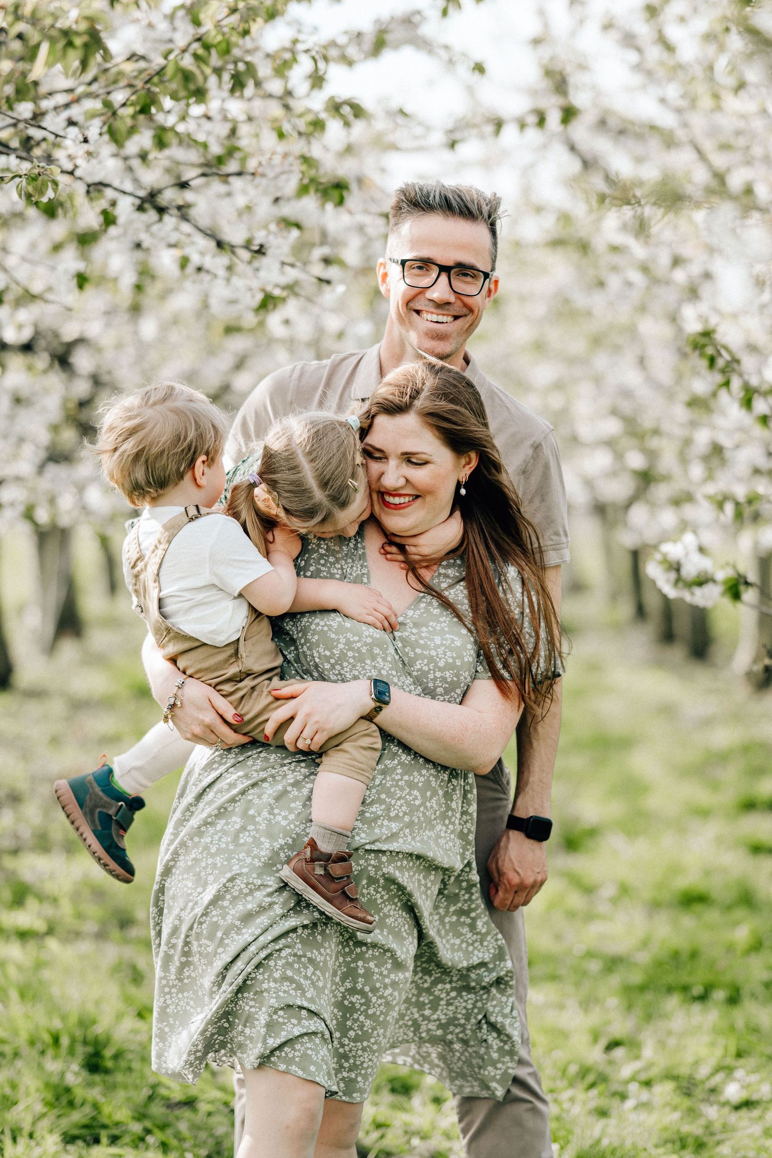 Family shares joyful moments together under blooming cherry trees in a spring orchard.
