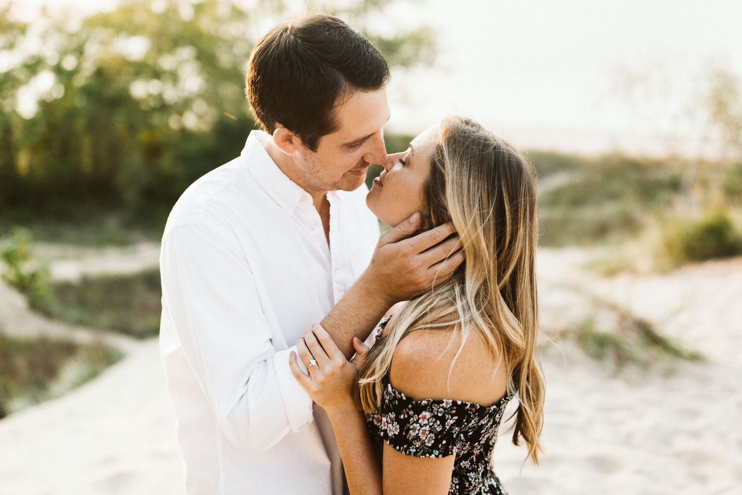 Romantic couple embracing on sandy beach at sunset with soft golden lighting and natural scenery.