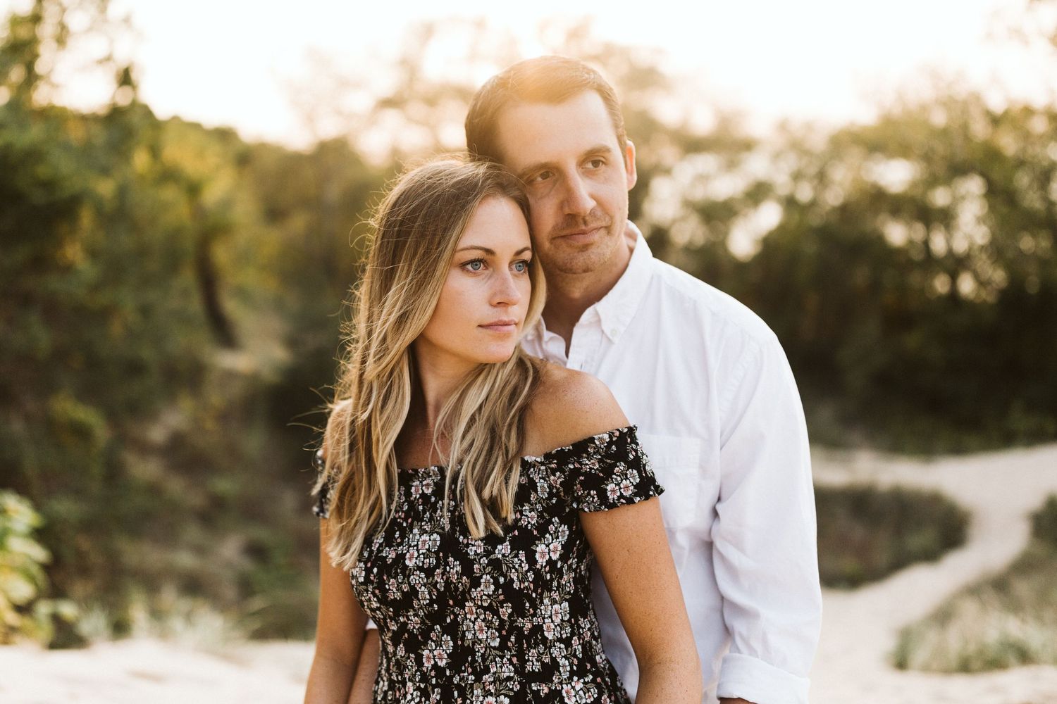 Romantic couple embraces on sandy beach dunes during golden hour sunset.